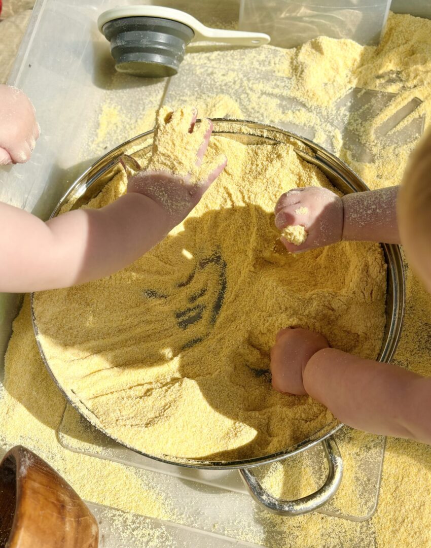 A child playing with yellow sand in a bowl.