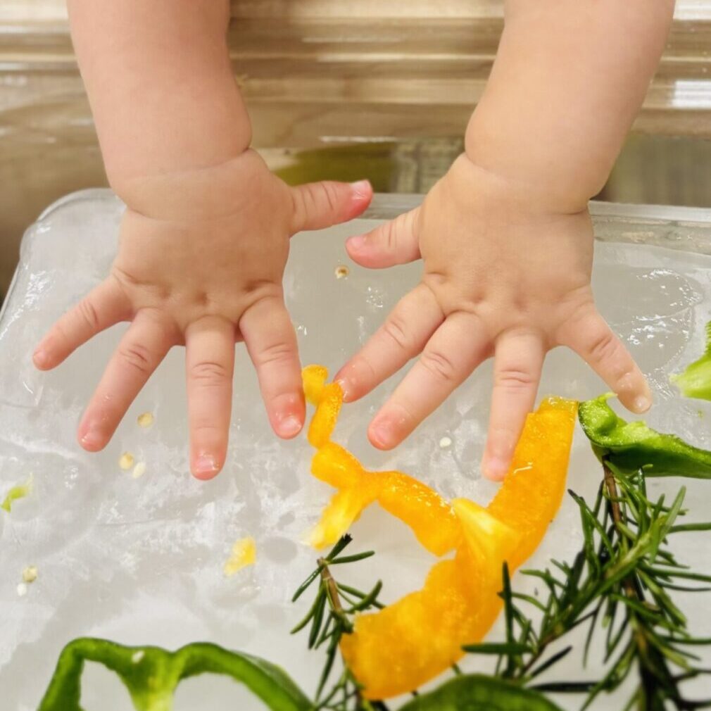 A child 's hands are playing with food on ice.